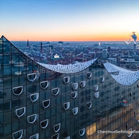 Ein Blick über das wellenförmige Dach der Elbphilharmonie Hamburg mit Stadtpanorama
