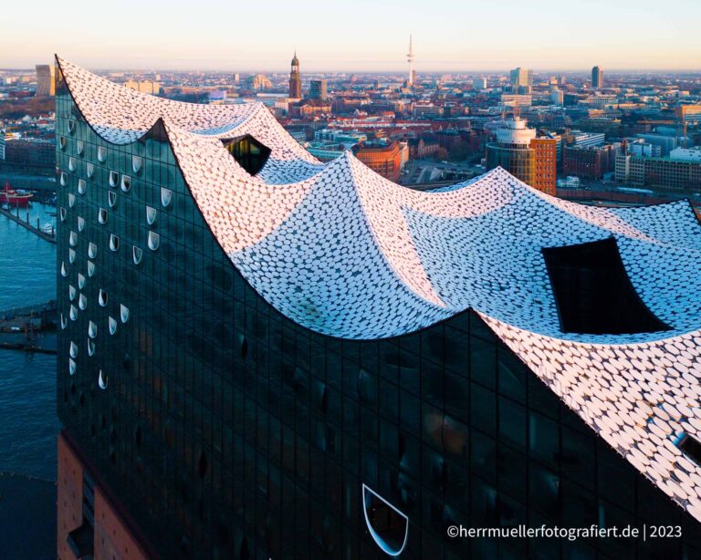 Ein Blick über das wellenförmige Dach der Elbphilharmonie Hamburg mit Stadtpanorama
