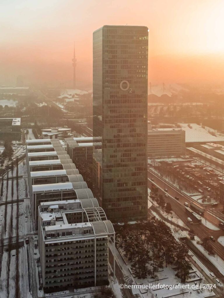 Der o2 Tower München mit Olympiaturm und -park in warmes Sonnenlicht getaucht