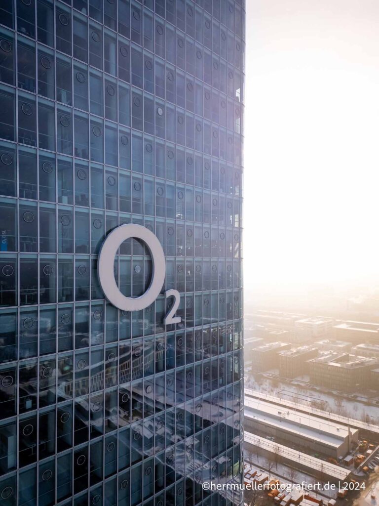 Der o2 Tower München mit o2 Markenlogo vor strahlender Sonnen